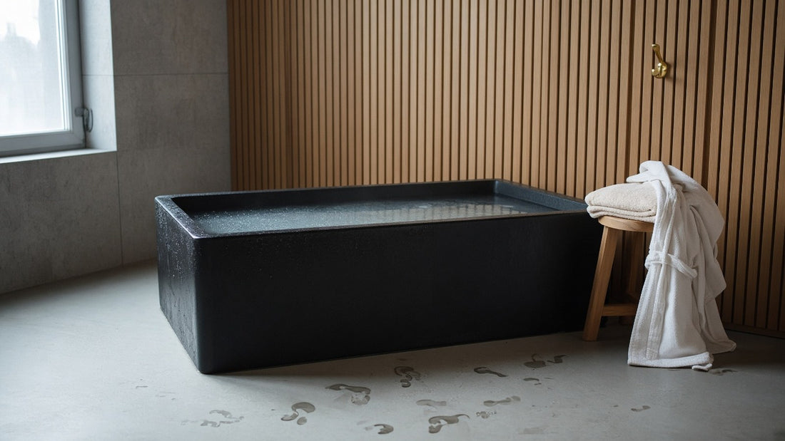  A cold plunge tub filled with clear water in a bright spa room with wood slat walls and a folded towel on a stool